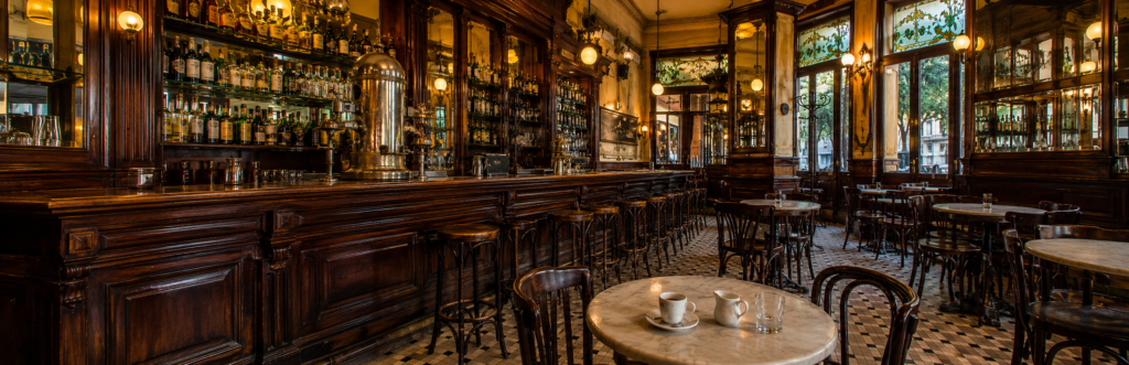 Interior de un bar histórico porteño con barra de madera, cafetera antigua y mesas de mármol.